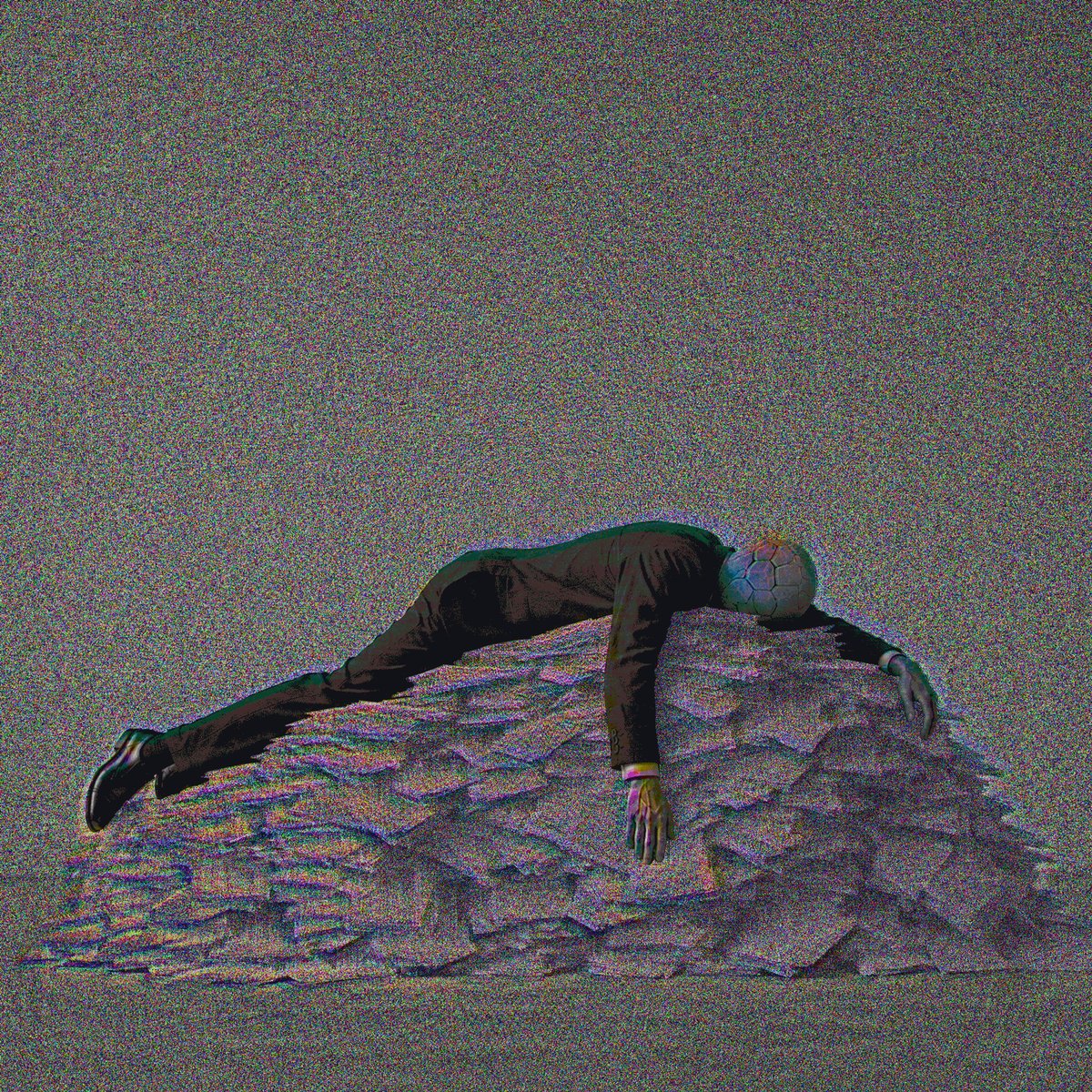The image features a man lying down on his stomach, with his arms and legs spread out over a pile of rocks or boulders. The background appears to be a gray sky, which contrasts with the man's dark clothing. There are no other objects in the scene, and the focus is solely on the man and the rock formation he is resting on.