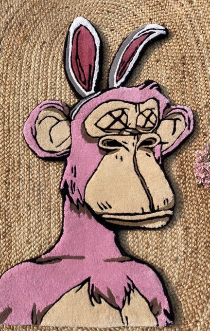 A hand-drawn illustration of a pink monkey with bunny ears and X's for eyes, drawn in black ink and colored with pink and tan hues, lying on a textured tan surface.
