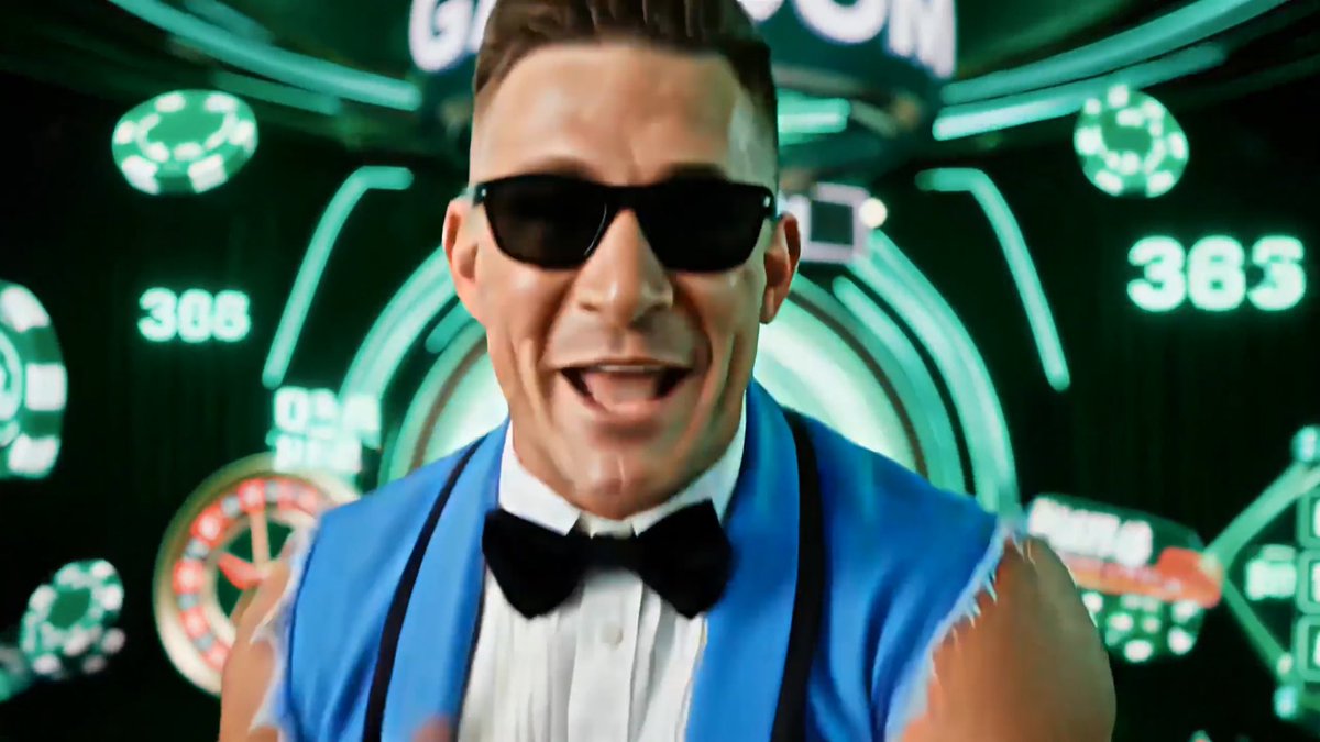 A man wearing sunglasses and a blue suit with a black bowtie is singing enthusiastically in front of a green neon background filled with casino-themed graphics and numbers.