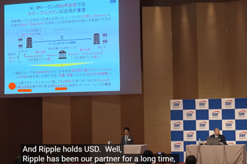 The image shows a presentation being held by two men, one standing behind a podium with a screen displaying information about Ripple currency and its potential benefits for investors. The other man is sitting at a table next to the speaker. The room has a large screen in front of them that displays text related to Ripple currency.