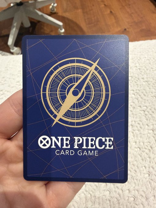 A person holds up a blue "ONE PIECE CARD GAME" deck box or card back featuring a gold compass logo, shown as part of a listing for an OP17 Luffy crew leader card. The post advertises the card for sale at $22,500, highlighting its pristine condition and willingness to ship or hand-deliver along the East Coast, with crypto as the preferred payment method.