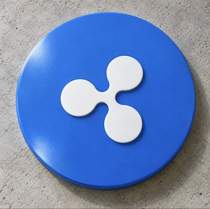 A blue circular Ripple (XRP) cryptocurrency logo with the white three-dobed symbol rests on a gray concrete surface.
