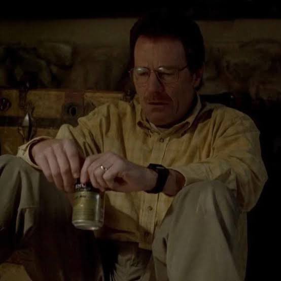 A still image of a bearded man with glasses in a yellow shirt, sitting and holding a can, resembling a scene from a TV show.