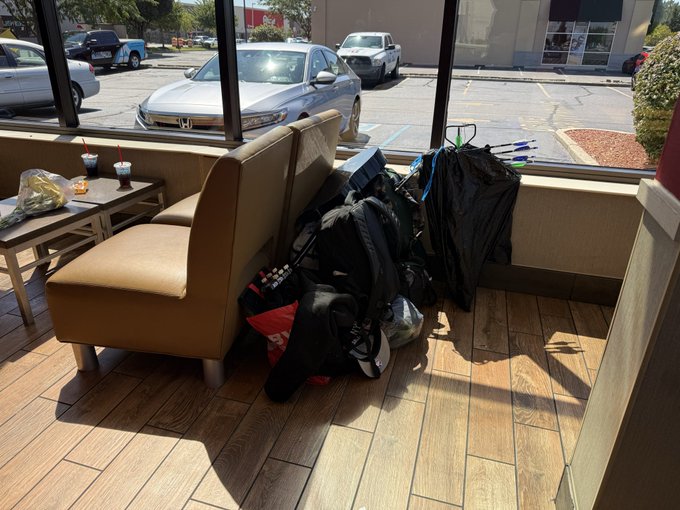 A pile of black bags, backpacks, and hangers sits haphazardly on a booth seat inside a fast-food restaurant.