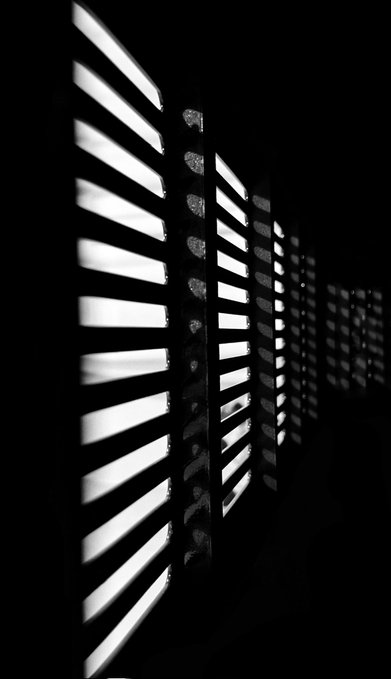 A high-contrast black and white photograph of a modern architectural structure, showing illuminated horizontal louvers receding into darkness against a night sky.