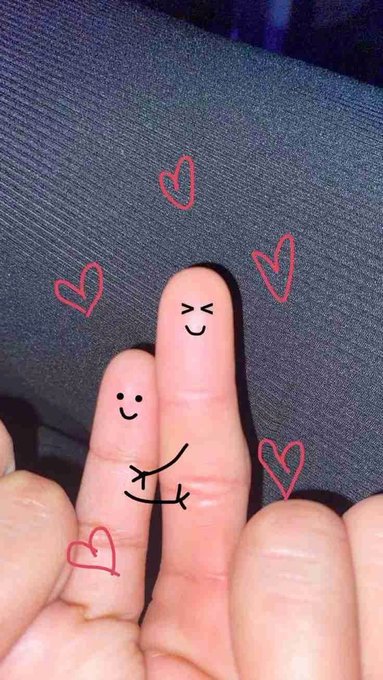 A close-up photo of a hand with doodled faces and hearts drawn around the fingers, creating an anthropomorphized scene.