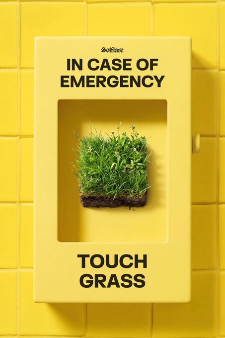 A bright yellow emergency-style cabinet mounted on a yellow-tiled wall displays the text "IN CASE OF EMERGENCY" above a patch of grass and "TOUCH GRASS" below, with the "Solflare" logo at the top. The image humorously plays on the internet phrase "touch grass" (meaning to take a break from the digital world and reconnect with reality), framing it as an emergency protocol—serving as a gentle reminder to log off and get outside.