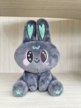 A gray plush bunny toy with star-shaped green accents on its ears and paws sits against a wooden background.