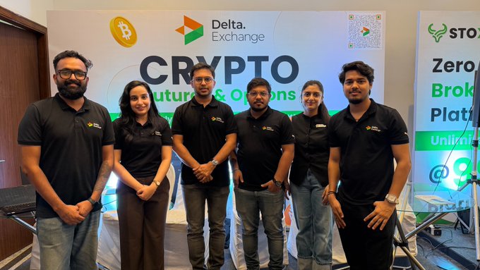 A group photo of six people in matching black polo shirts posing at what appears to be a Delta Exchange event about 'CRYPTO Futures & Options'.