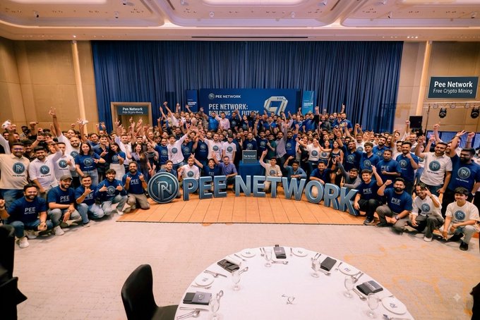 A large group of Pee Network community members gather in coordinated navy and white branded shirts in front of a "Pee Network: Holders & Miners" stage backdrop, with many attendees posing behind the prominent 3D "PEE NETWORK" lettering to showcase the global community of miners behind the $PN token.