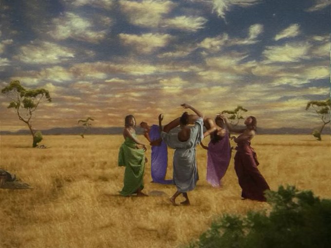 Five women in flowing, vibrant dresses dance in a circle across a golden savanna under a dramatic, cloud-streaked sky. The scene's sweeping natural setting and fluid motion evoke a timeless celebration of nature's rhythm, fitting the "Dance of Seasons" theme.