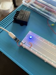 A breadboard circuit with a USB connector, a blue LED lit, and a black power supply unit indicates successful pump wiring as evidenced by the glowing LED.