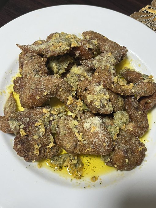 A white plate holds pieces of breaded, pan-fried meat drizzled with a yellow sauce or melted butter, possibly a homemade chicken or liver dish.