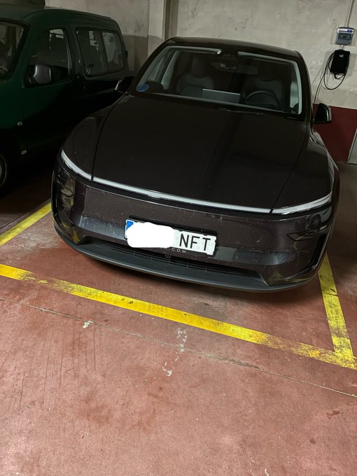 A dark gray/black electric vehicle (appears to be a Polestar 2) parked in an indoor garage with yellow parking lines, featuring a custom license plate reading "NFT" with the rest whited out.