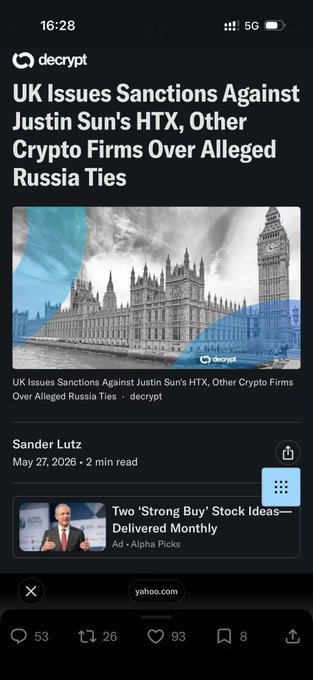The image features a cell phone screen displaying a news article from the Decrypt blog titled "UK Issues Bans on Cryptos. Other crypto firms over Allied alleged". The text appears in both English and Russian, with the headline written in multiple languages. The article discusses the UK government's recent restrictions on cryptocurrency exchanges, detailing issues faced by these exchanges due to UK regulator scrutiny. The content seems to focus on the risks associated with cryptocurrency trading and the potential compliance challenges that have arisen for users who use such platforms.