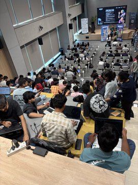 A large room full of people sitting on the floor with laptops and tablets, appearing to be at a gaming or tech event.