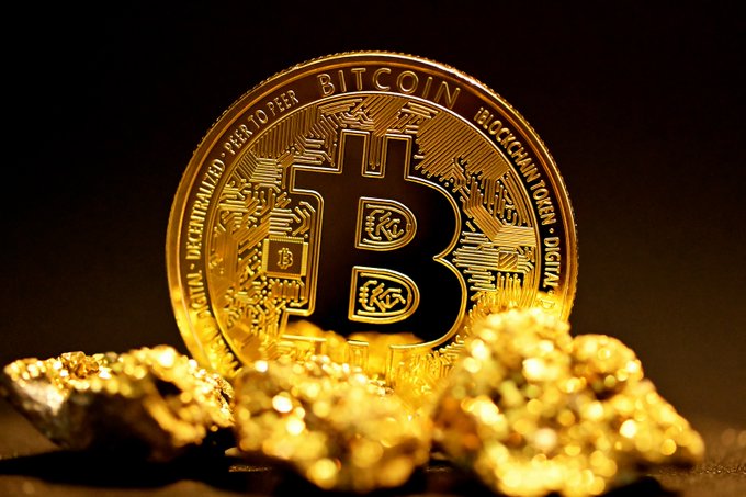 A gleaming gold Bitcoin coin with "BITCOIN," "PEER TO PEER," and "DIGITAL" inscribed on it stands upright among scattered gold nuggets, visually reinforcing the article's message about Bitcoin's "digital gold" thesis holding strong near $60K.