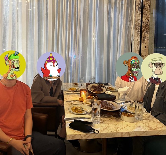 A group of people dining at a restaurant with their faces covered by NFT-style cartoon avatars, including Bored Ape characters, with food spread across a marble table.