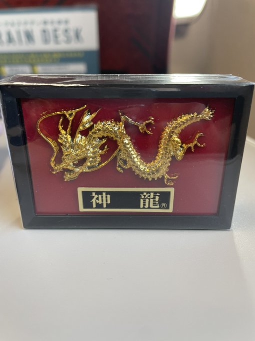 A gold dragon figurine mounted on a red plaque with Chinese characters 神龍 (Shen Long) displayed on a Train Desk surface.