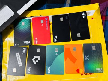 A collection of various Visa bank cards in different designs and colors arranged on a yellow surface, including black, red, green, and orange cards with different logos.