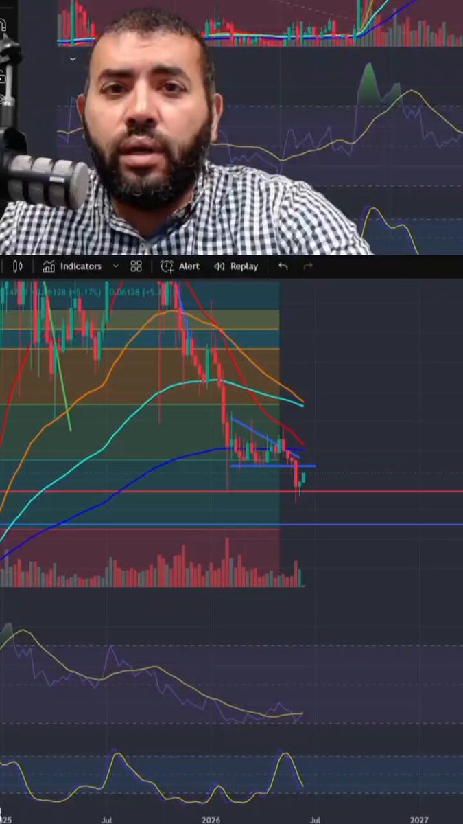 A man wearing a checkered shirt with a beard is sitting behind a computer screen, which appears to be of some sort related to Bitcoin or another cryptocurrency. There are charts displayed on his computer screen showing fluctuations in the value of the Bitcoin currency over time. The chart displays a downward trend towards the right side and has been updated every day since it was first recorded. It seems that this man is closely monitoring the price changes, possibly as an investment or for other reasons related to cryptocurrency.
