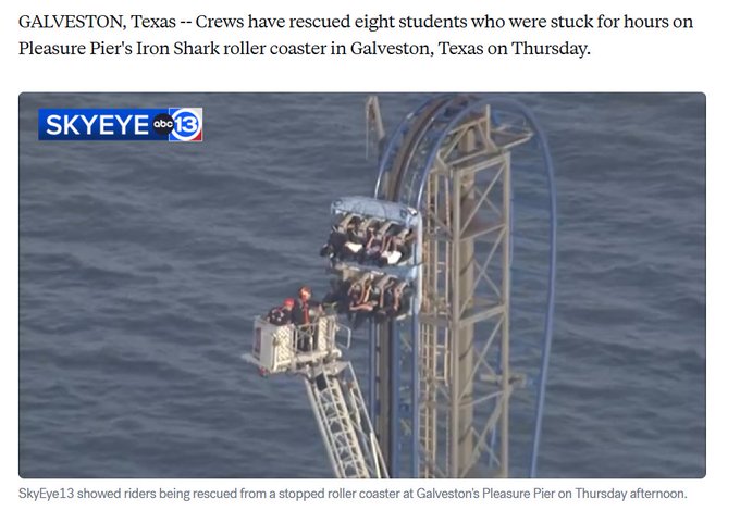 The image shows a roller coaster with people riding it from an aerial view. There are several riders visible on the roller coaster, including one person who appears to be hanging off the side of the ride. The roller coaster is located at Galveston, Texas, and has been described as being "stuck for hours" due to a mechanical issue or accident.