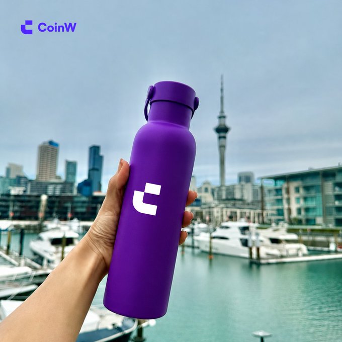 A hand holds up a purple CoinW branded water bottle in front of a scenic harbor cityscape with boats and a tall tower, promoting the message "Take CoinW wherever you go."