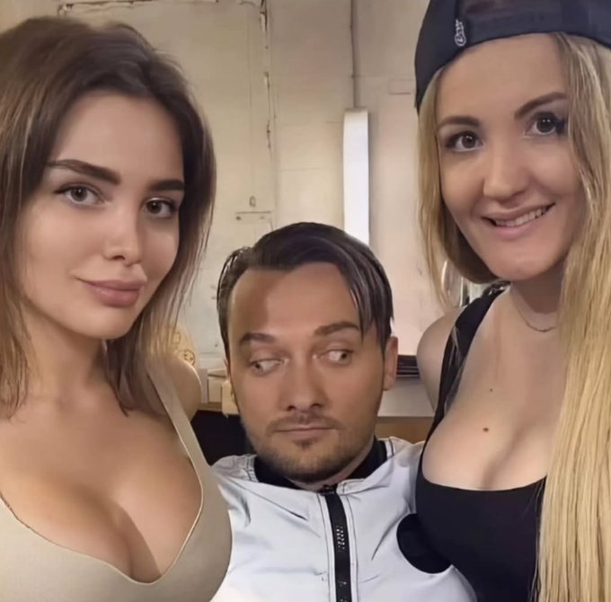 A man sits between two smiling women who lean in close to him for a selfie, all looking at the camera.