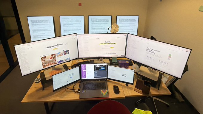 An elaborate multi-monitor workstation featuring three large curved monitors and a laptop, displaying text including 'Shop with Frevo' and 'Got your website' along with code on the screens.