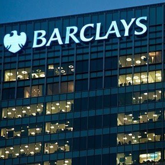 A nighttime photograph of a tall building with the illuminated white "BARCLAYS" logo and eagle emblem prominently displayed on its dark glass facade.