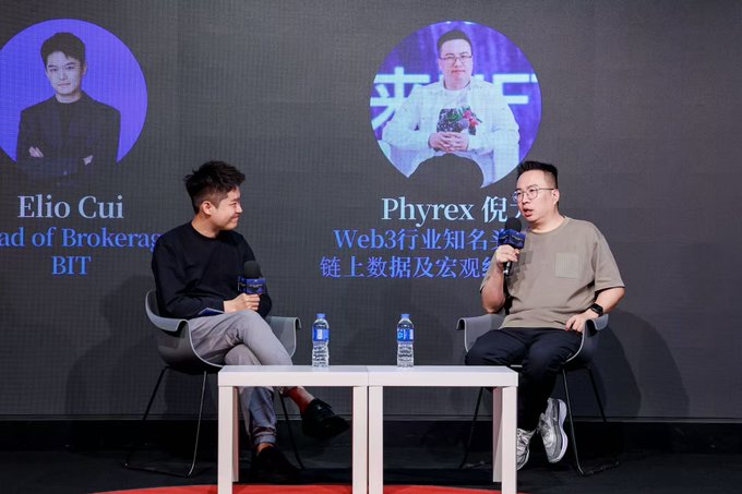 Two men sit on stage in chairs holding microphones during a panel discussion at a BIT brokerage forum, with a large backdrop screen displaying their photos and titles: "Elio Cui, Head of Brokerage, BIT" on the left and "Phyrex 倪" (Web3 industry influencer specializing in on-chain data and macroeconomics) on the right, matching the post about a substantive discussion covering monetary policy, stablecoins, and position management discipline.