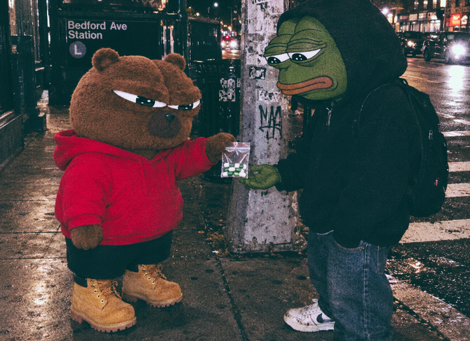Two people in mascot costumes—one in a brown bear hoodie with a red sweatshirt and Timberland boots, the other in a green Pepe the Frog mask with a black hoodie—stand on a city street near a "Bedford Ave Station L" sign, exchanging a small bag.