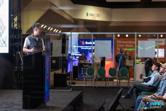 Lin Yao, co-founder of TLAY, delivers a presentation titled "Building the Economic Infrastructure for Physical AI" at the AI Infra Summit 2026, standing at a podium while seated attendees listen attentively in a conference hall setting.