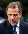 A low-resolution close-up photo of a middle-aged man with gray hair and a beard, wearing a dark suit, looking downward with a serious expression.