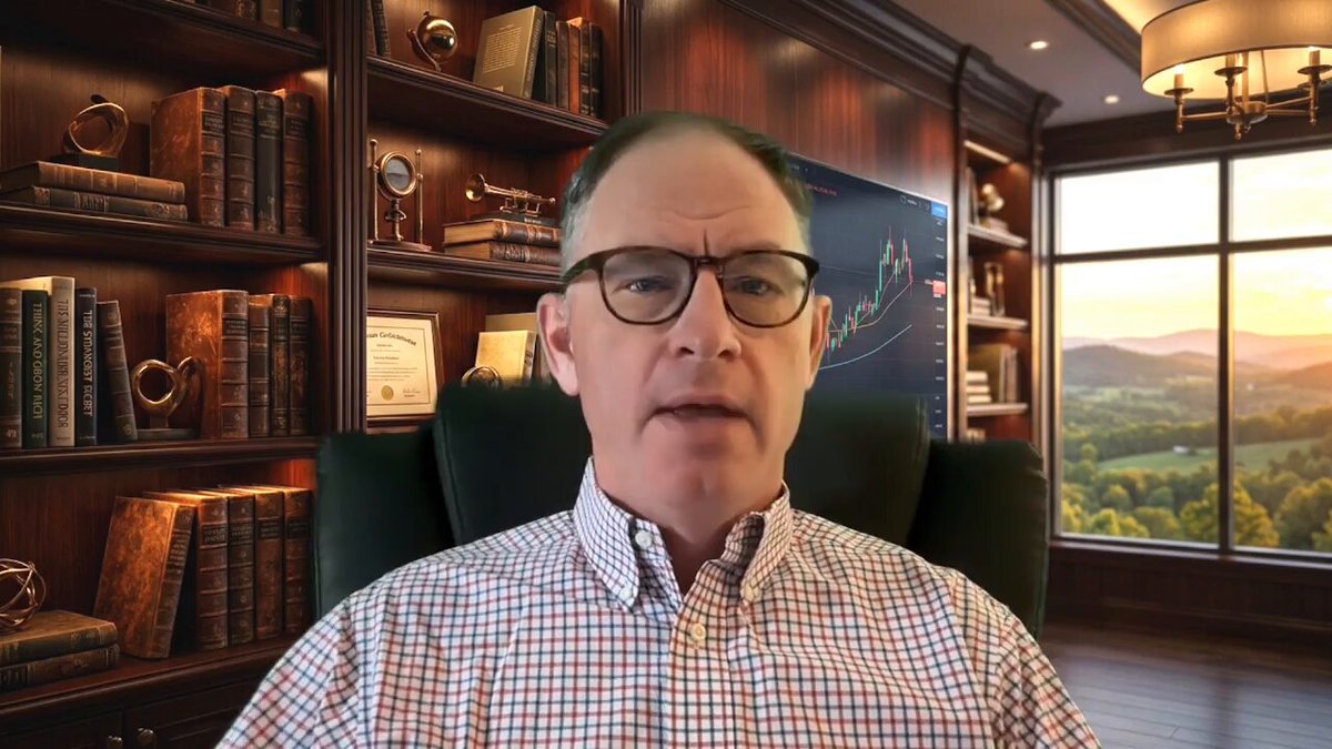 The image features a man sitting in an office chair, wearing glasses and a plaid shirt. He appears to be giving a presentation or speaking into a camera. The background of the image shows a bookshelf filled with numerous books, suggesting that he might be working in a library or a professional setting related to finance or investments.