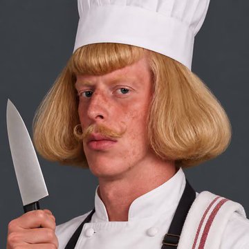 A person dressed as Chef Boyardee, wearing a chef's hat, blonde bob wig, mustache, and white uniform, holding a large kitchen knife.