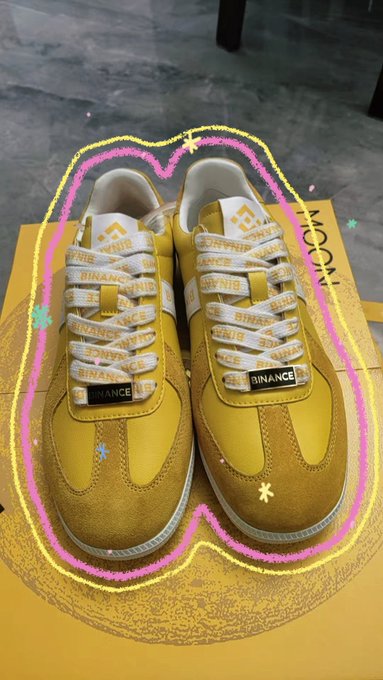 A pair of yellow sneakers featuring repeating "BINANCE" branding across the laces and tongue are displayed on a Binance-branded box, celebrating the Mid-Autumn Festival with a stylish citywalk-ready crypto fashion statement. The hand-drawn heart overlay emphasizes the wearer's excitement over the exclusive Binance merchandise.