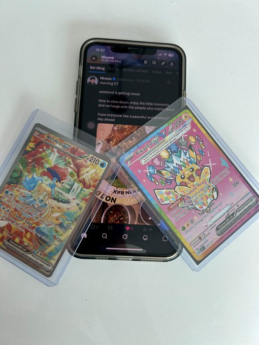 A smartphone displaying a Hirono Instagram post ("morning CT - weekend is getting closer") rests beneath two protected Pokémon cards—a "Wailord ex" (210 HP) and a Radiant "Blaziken" (200) — symbolizing how sleek digital infrastructure (Renaiss) could one day authenticate and trade rare physical collectibles like these graded cards.
