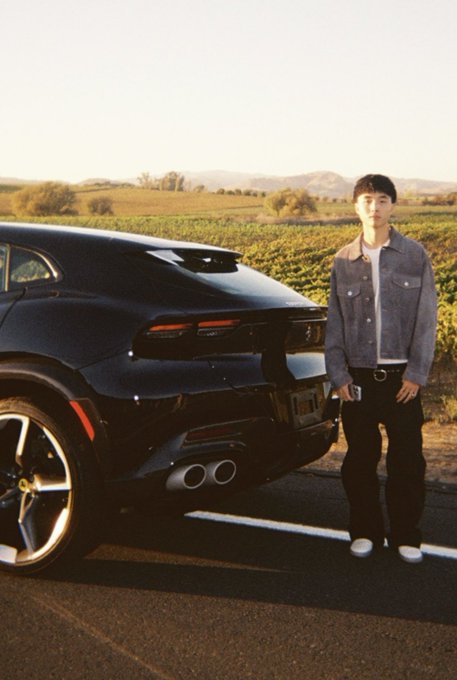A man identified in the post as “Kimchi” stands beside a black Ferrari SUV in a sunlit field with hills in the background. No readable vehicle text or other clear text is visible; the post presents him as a wealthy crypto trader connected to Pump.fun.