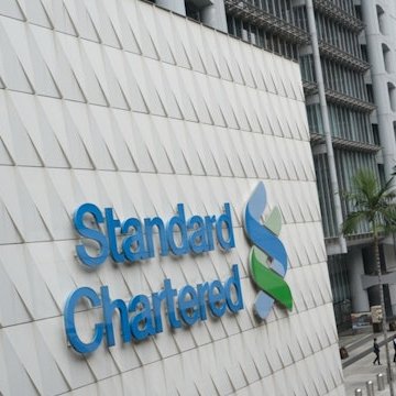 A photo of the Standard Chartered bank logo mounted on the exterior of a building with a tiled facade.