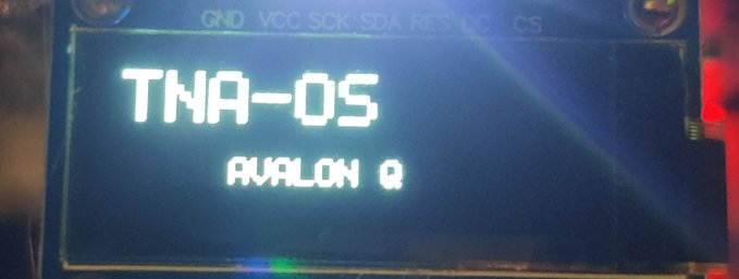 A small LCD display screen showing the text 'TNA-OS' with 'AVALON Q' below it, set against a circuit board background with labels including GND, VCC, SCK, SDA, RES, DC, and CS.