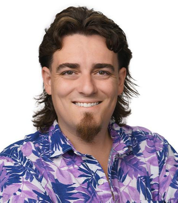 A portrait of a smiling man with shoulder-length brown hair, a goatee, and a purple tropical-print shirt against a white background.