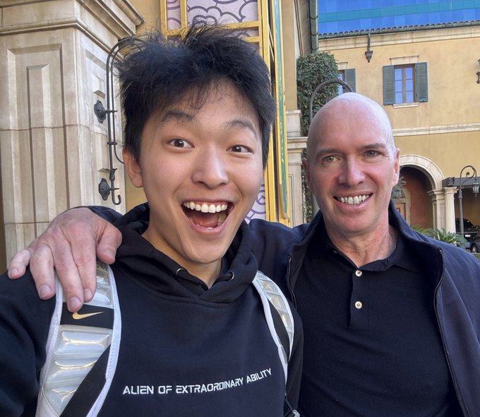 A joyful young man wearing a hoodie that reads "ALIEN OF EXTRAORDINARY ABILITY" poses for a selfie alongside a smiling older man, appearing to capture a moment of collaboration with the a16z team.