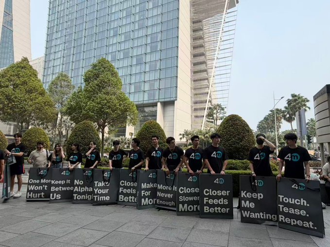 A group of male models wearing matching "4D" t-shirts pose with promotional signs reading "One More Keep It Won't Hurt Us," "No Alpha Tonight," "Close Feels Better," "Make More For Never Enough," "Close Slower," "Keep Me Wanting," and "Touch. Tease. Repeat."—appearing to be a marketing stunt for 4M Exchange that leveraged attractive models to stand out in the competitive traffic wars.