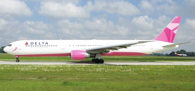 A Delta Airlines passenger jet with a white fuselage, pink underbelly, and pink geometric tail livery parked on an airport tarmac under a partly cloudy sky.