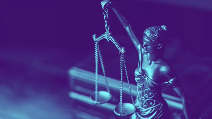 A blue-tinted photograph of a Lady Justice statue holding balanced scales, symbolizing law and fairness.