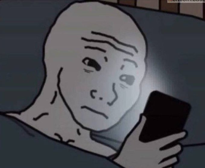 A cartoon drawing of a bald man lying in bed looking at a phone screen in the dark.