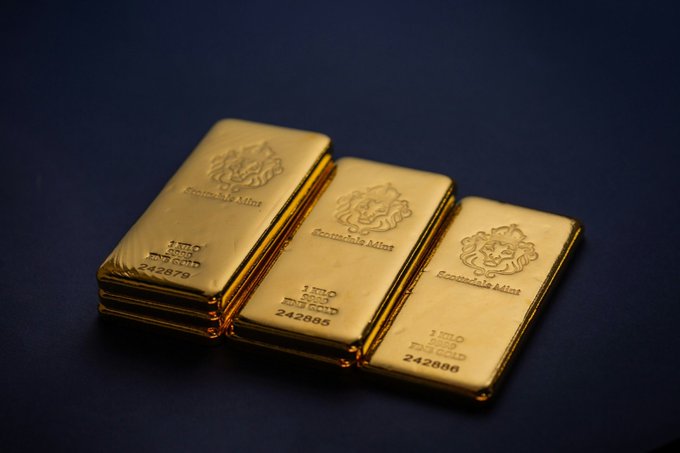 Three stacks of 1-kilo fine gold bars from 'Scottsdale Mint' with serial numbers 242879, 242885, and 242886 arranged on a dark blue background.