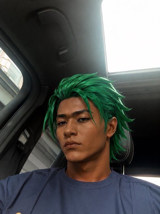 A digitally rendered or cosplayed character with bright green spiky hair sitting inside a car, looking toward the camera.