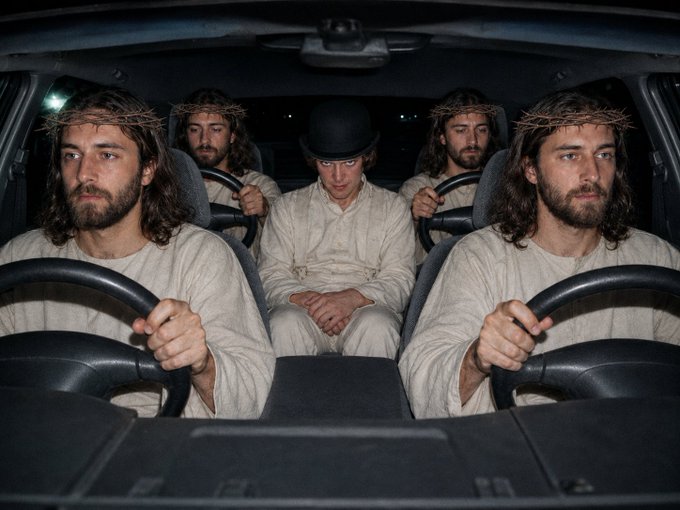 Four men dressed in white robes and wearing crown-of-thorns headbands sit inside a car, with two of them holding the steering wheels.